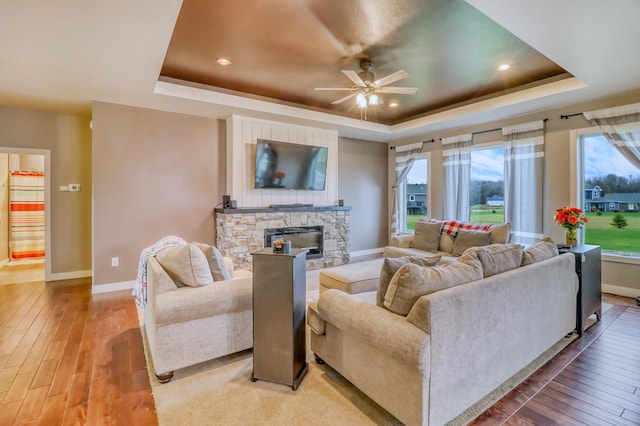 living room featuring baseboards, light wood-style flooring, ceiling fan, and a tray ceiling