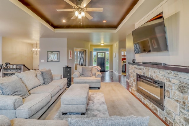 living room featuring a raised ceiling, a fireplace, ceiling fan with notable chandelier, recessed lighting, and wood finished floors