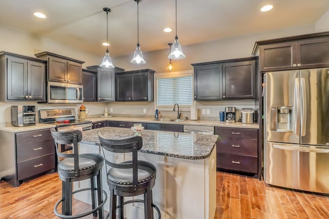 kitchen featuring a sink, light wood finished floors, appliances with stainless steel finishes, and a kitchen bar