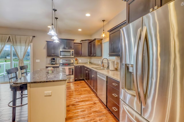 kitchen featuring appliances with stainless steel finishes, a sink, light wood finished floors, a breakfast bar area, and a center island