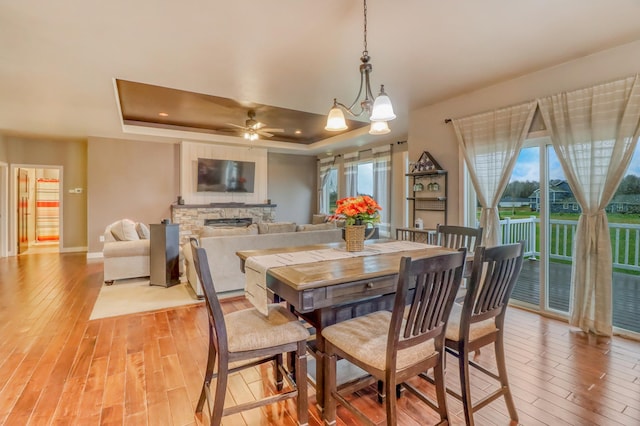 dining room with baseboards, light wood finished floors, ceiling fan, and a tray ceiling