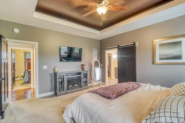 carpeted bedroom with baseboards, a glass covered fireplace, a barn door, and a raised ceiling