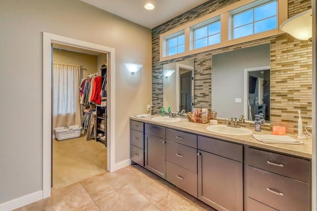 full bathroom featuring baseboards, double vanity, a walk in closet, and a sink