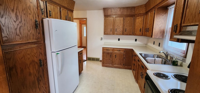 kitchen featuring brown cabinetry, a sink, light floors, under cabinet range hood, and white appliances