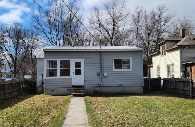back of property featuring entry steps, a yard, a fenced backyard, and metal roof