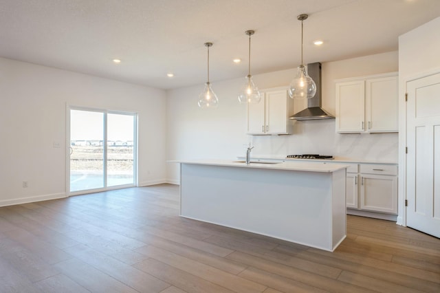 kitchen featuring white cabinets, a sink, light countertops, wall chimney exhaust hood, and wood finished floors
