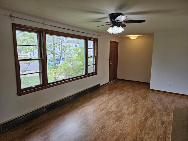 empty room with a baseboard heating unit, ceiling fan, wood finished floors, and baseboards
