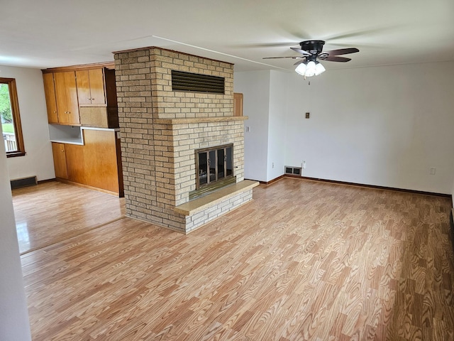 unfurnished living room with light wood finished floors, a ceiling fan, a brick fireplace, and baseboards