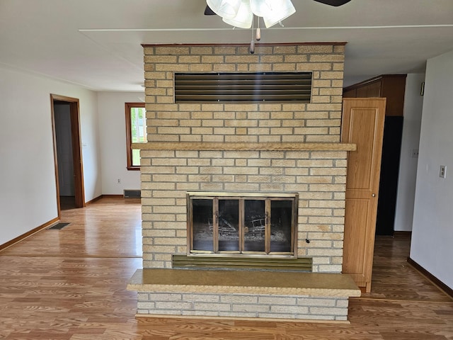 detailed view of a fireplace, a ceiling fan, wood finished floors, and baseboards