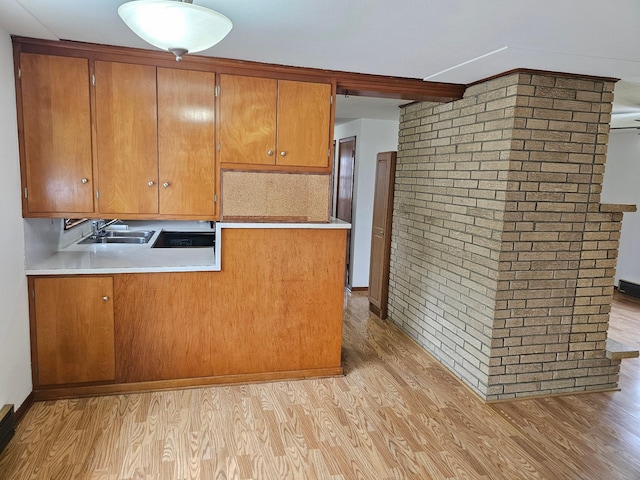kitchen with light wood-type flooring, a sink, brown cabinetry, light countertops, and brick wall