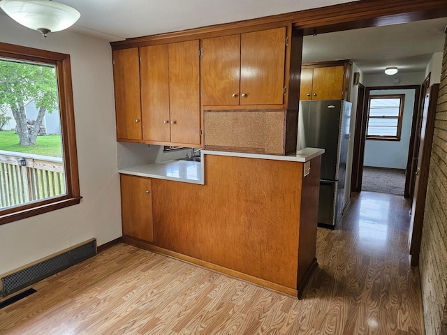 kitchen featuring freestanding refrigerator, light wood-style floors, brown cabinetry, light countertops, and tasteful backsplash