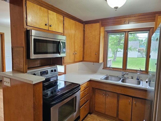 kitchen featuring stainless steel appliances, a sink, brown cabinets, light countertops, and light wood-style flooring