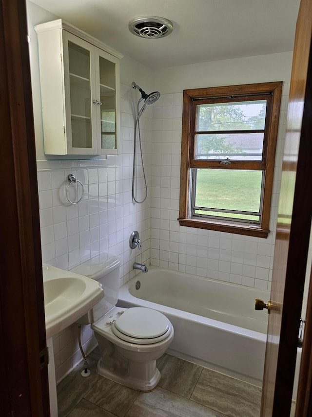 bathroom featuring toilet,  shower combination, tile patterned floors, and tile walls