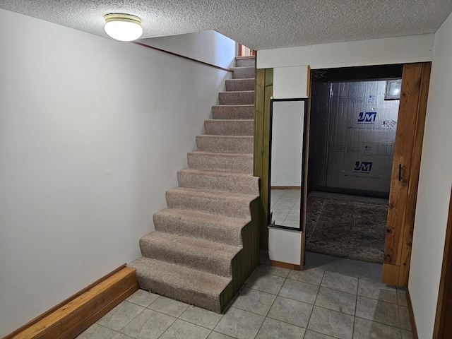 stairway featuring a textured ceiling, tile patterned floors, and baseboards