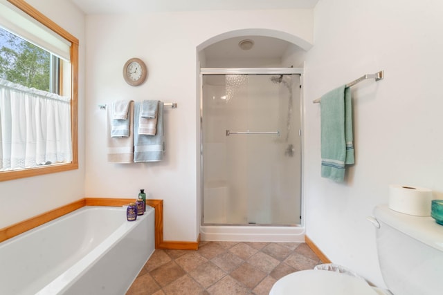 bathroom featuring stone finish floor, a garden tub, a stall shower, baseboards, and toilet