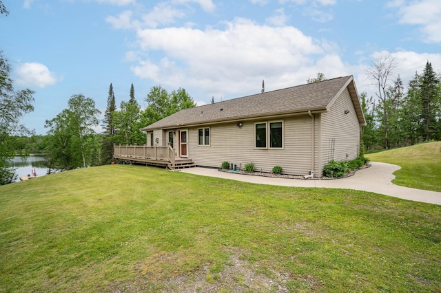 back of property with a deck with water view, a lawn, and roof with shingles