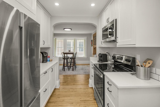 1449 Laurel Ave, Saint Paul, MN 55104 - kitchen featuring appliances with stainless steel finishes, light wood-style flooring, arched walkways, white cabinets, and recessed lighting
