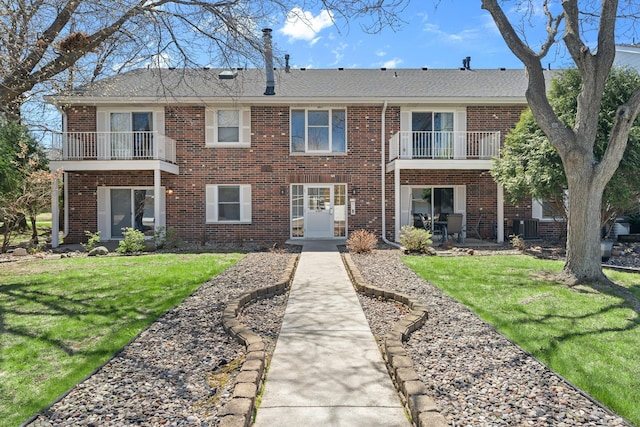 view of front of home featuring central air condition unit, brick siding, a balcony, and a front yard
