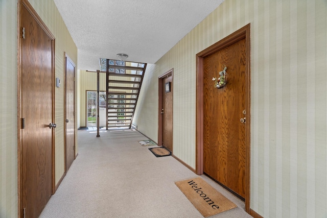 corridor with light colored carpet, a textured ceiling, and wallpapered walls