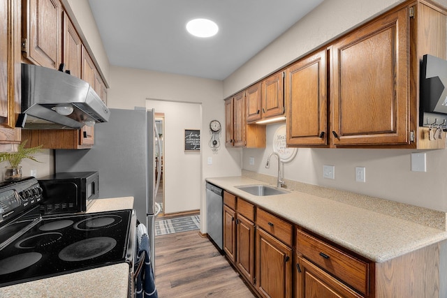 kitchen featuring wood finished floors, ventilation hood, brown cabinets, a sink, and black appliances