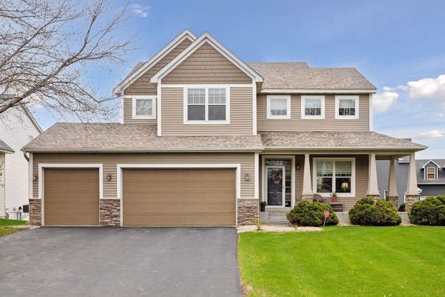 craftsman-style house featuring a front lawn, asphalt driveway, covered porch, a garage, and stone siding