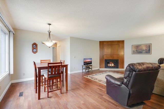dining room featuring visible vents, wood finished floors, a healthy amount of sunlight, and a large fireplace