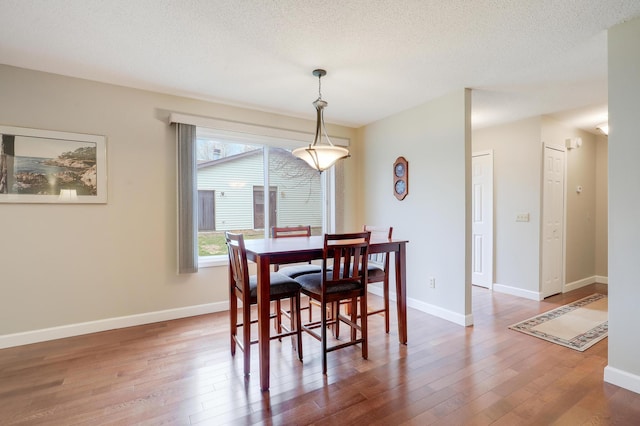 dining area featuring a textured ceiling, baseboards, and wood finished floors