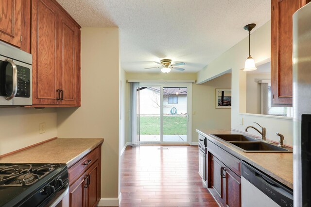 kitchen featuring brown cabinetry, dishwashing machine, a textured ceiling, stainless steel microwave, and a sink