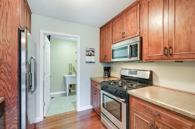 kitchen with brown cabinetry, wood finished floors, light countertops, baseboards, and stainless steel appliances