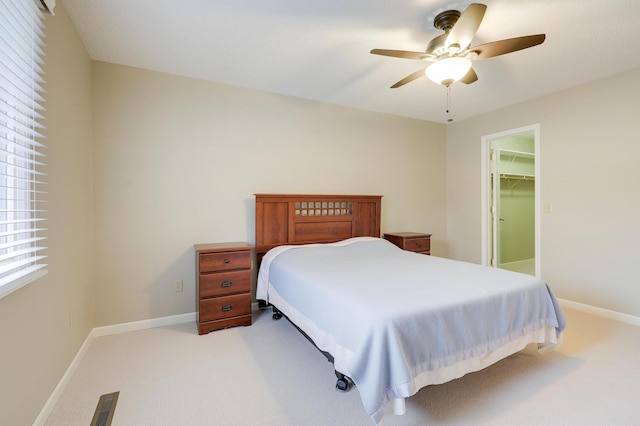 bedroom featuring light colored carpet, baseboards, a walk in closet, and ceiling fan