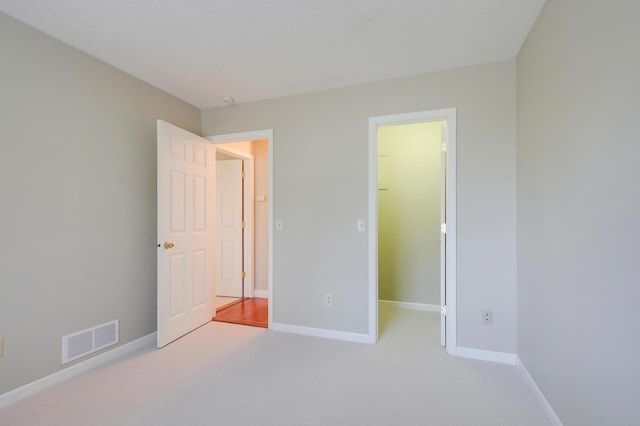 unfurnished bedroom with visible vents, a closet, baseboards, a walk in closet, and carpet flooring