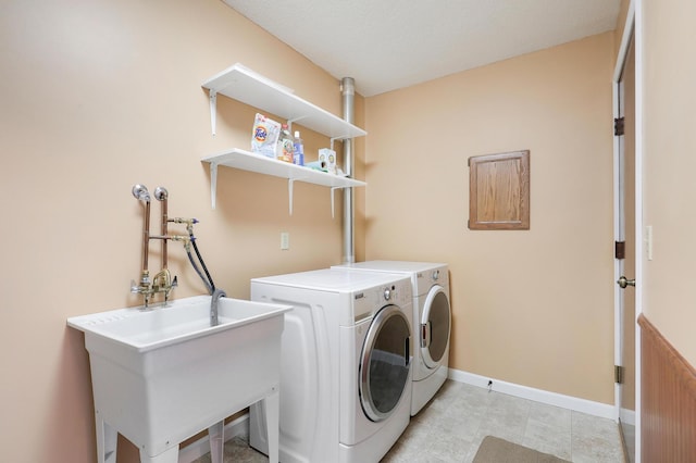clothes washing area featuring laundry area, a sink, baseboards, and washing machine and clothes dryer