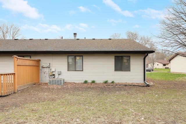 rear view of property with central AC unit, a shingled roof, and a yard