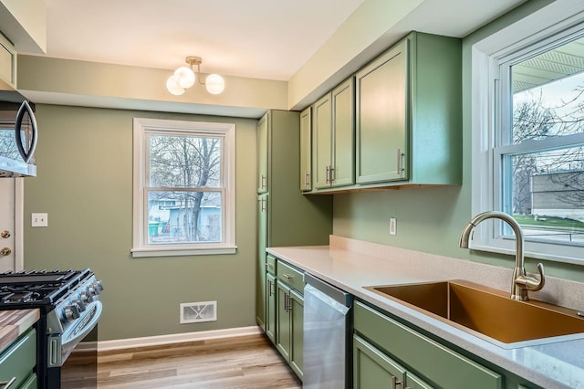kitchen with visible vents, a sink, green cabinets, light wood finished floors, and stainless steel appliances
