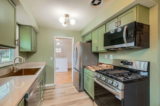 kitchen featuring baseboards, a sink, light wood-style flooring, green cabinets, and stainless steel appliances