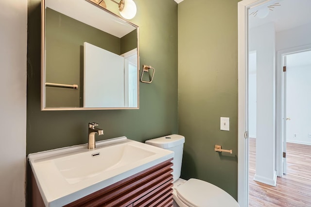 half bathroom featuring toilet, baseboards, wood finished floors, and vanity