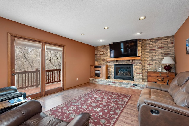living area featuring a brick fireplace, a textured ceiling, and wood finished floors