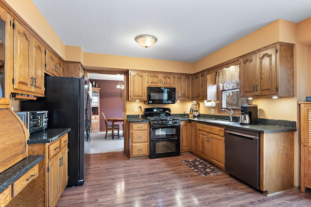 kitchen with dark countertops, brown cabinets, dark wood finished floors, a sink, and black appliances