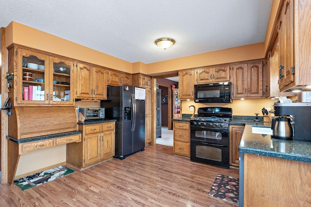 kitchen with brown cabinets, dark countertops, a textured ceiling, light wood-style flooring, and black appliances