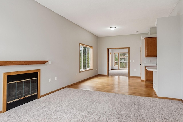 unfurnished living room featuring baseboards, a glass covered fireplace, light carpet, and light wood finished floors