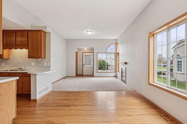 kitchen featuring visible vents, brown cabinetry, light wood-type flooring, light countertops, and a sink