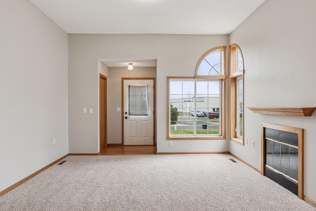 unfurnished living room featuring carpet floors, baseboards, a glass covered fireplace, and visible vents