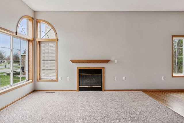 unfurnished living room featuring visible vents, baseboards, a glass covered fireplace, and a wealth of natural light