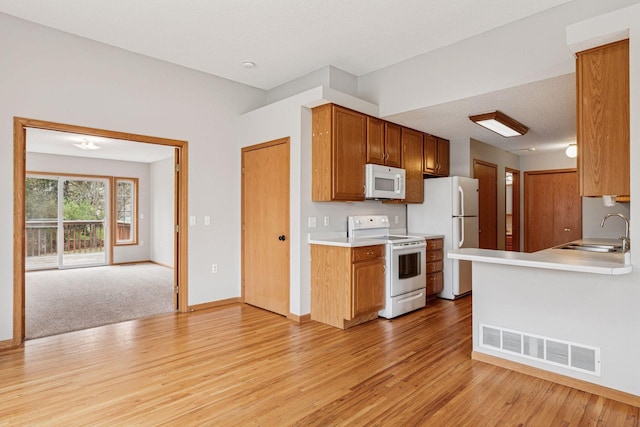 kitchen featuring visible vents, white appliances, light countertops, a sink, and light wood finished floors