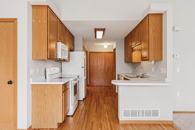 kitchen featuring visible vents, a sink, light countertops, white appliances, and light wood-style flooring