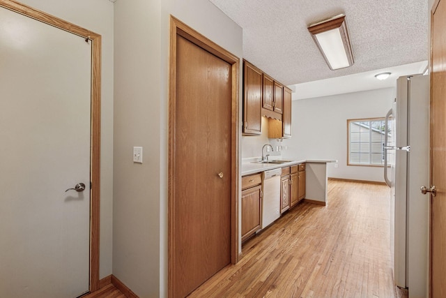 kitchen featuring a textured ceiling, light wood-type flooring, a sink, light countertops, and white appliances
