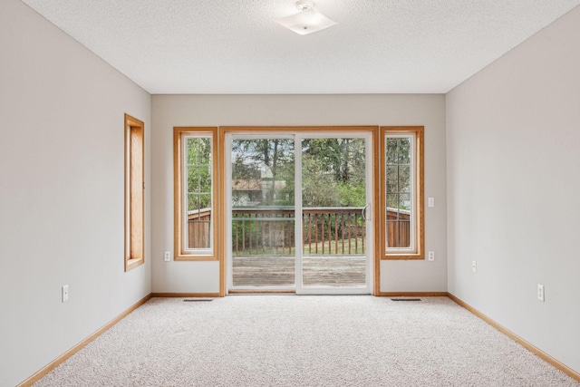 carpeted empty room featuring a textured ceiling, baseboards, and visible vents