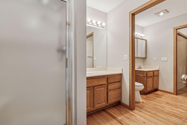 full bath with a sink, two vanities, wood finished floors, and a stall shower