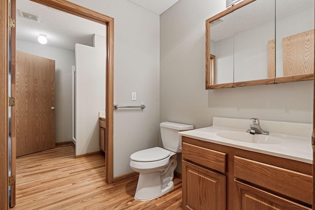 bathroom featuring a textured ceiling, visible vents, wood finished floors, vanity, and toilet