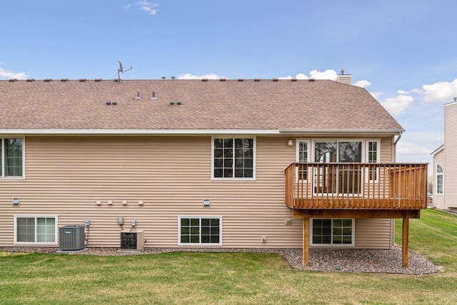 rear view of property with a wooden deck, a chimney, central AC unit, a shingled roof, and a lawn